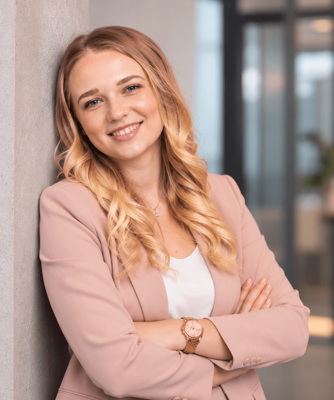 Porträt von Dajana Wiebe mit verschränkten Armen, lächelnd an eine Wand im Büro gelehnt